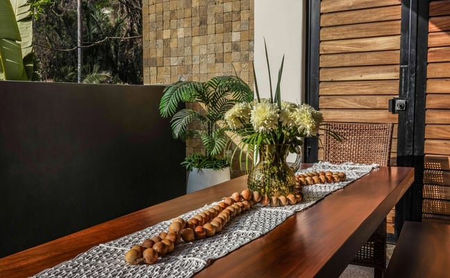 Covered patio with wooden table, hammock with cushions, and view of courtyard with flowering trees